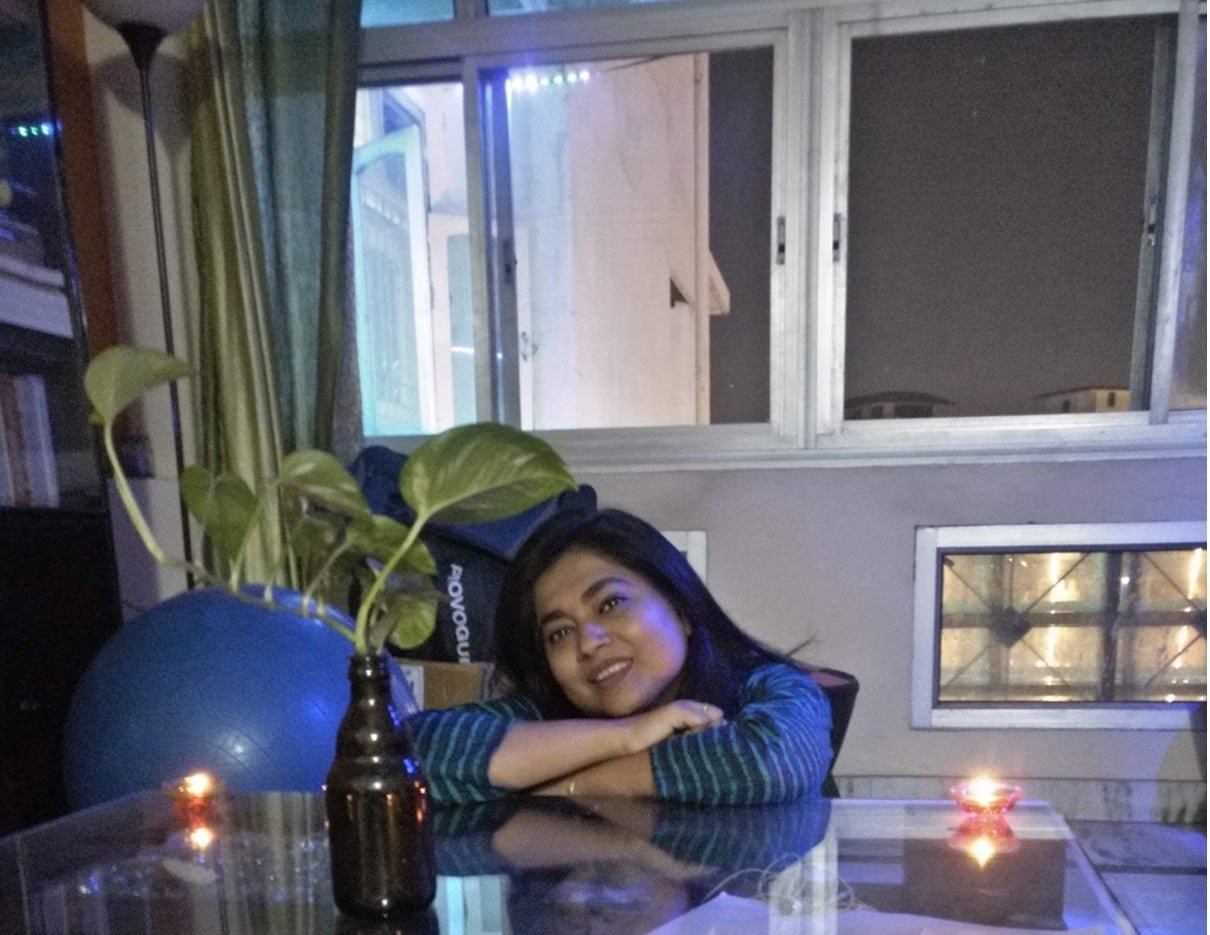 A woman seated at a clear kitchen table with large windows in the background.